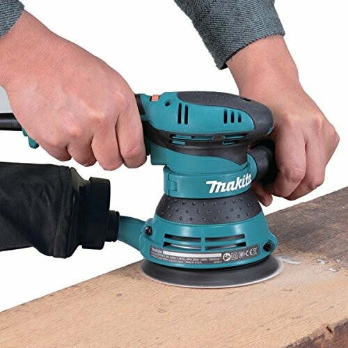 Person using a Makita orbital sander on wood